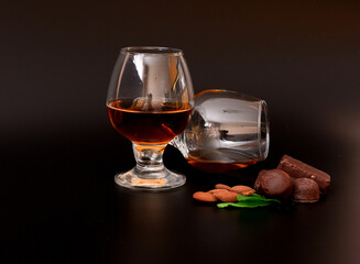 Cognac in two glasses, almonds, chocolates and mint leaves on a black background.