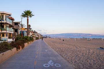 a long smooth bike path along the beach with people riding bikes surrounded by silky brown sand and beachfront homes and lush green palm trees and plants in Manhattan Beach California USA