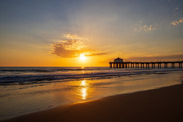 Fototapeta na wymiar a gorgeous summer landscape at the Manhattan Beach Pier with a stunning sunset in the sky with blue ocean water and waves rolling into the silky brown sand on the beach in Manhattan Beach California