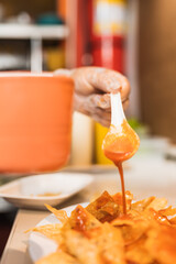 Vertical photo of the hand of a cook spreading sauce on nachos