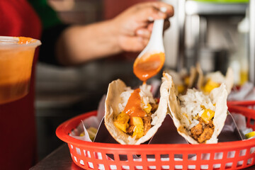 Worker pouring sauce on tacos in a basket to serve in a restaurant