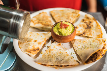Cook seasoning with pepper a plate of tacos ready to be served in a restaurant