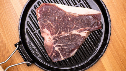 Top view, black meat roasting pan laying on a wooden table and a piece of raw meat.