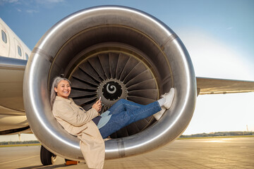 Cheerful woman with cellphone lying in aircraft engine