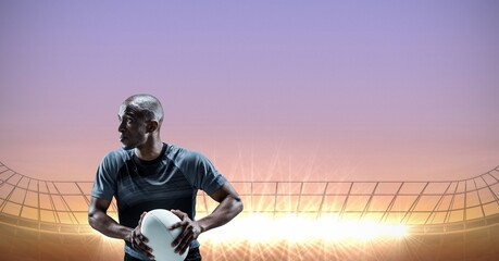 Composition of male rugby player holding rugby ball over sports stadium