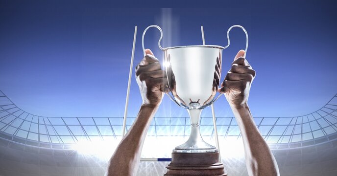 Composition of male rugby player celebrating victory, holding trophy on rugby pitch at stadium