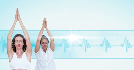 Two caucasian women performing yoga against heart rate monitor with copy space on blue background