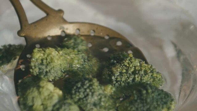 An old ladle with holes scoops broccoli out of the water and drains it