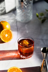 Photo of a Negroni cocktail glass with sun light and shadow and orange