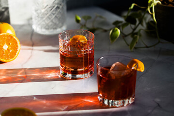 Photo composition of two Negroni glass cocktail with sun light and shadow and orange