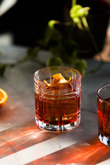 Photo composition of two Negroni cocktail glass with sun light and shadow and orange