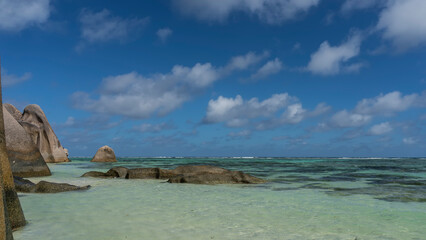 There are giant rounded boulders on the beach and in the ocean. Clear turquoise water and blue sky with clouds. Seychelles. La Digue Island. Anse Source D&rsquo;Argent beach