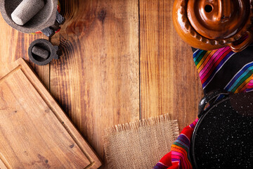 Mexican food cooking background with empty cutting board, colorful traditional fabric and molcajete...