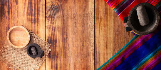 Mexican food cooking background with colorful traditional fabric and empty molcajetes on rustic wooden table. Panoramic top view with copy space.