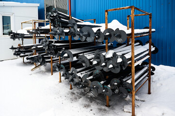 Helical piles on rusty metal rack in snowy warehouse yard