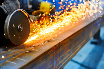 Worker cuts metal beam with abrasive disk in plant workshop