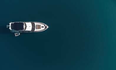 Fototapeta premium Aerial yacht on calm sea. Luxury cruise trip. View from above of white boat on deep blue water. Aerial view of rich yacht sailing sea. Summer journey on luxury ship.