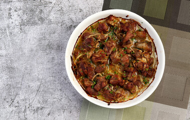Braised pork with onions  in a white baking dish on a dark grey background. Top view, flat lay