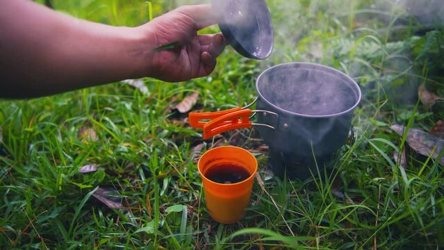 Footage of hand opening bowl with boiling water at alcohol base stove on green grass with blurry background. coffee time