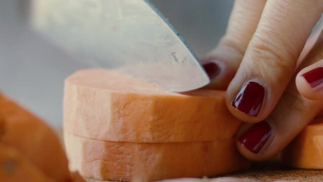 Detail of a hand cutting a sweet potato with a large knife in slow motion
