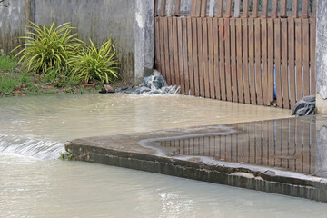 Flood water pours from inside a gate through and over sandbags out onto a driveway and gushes onto...