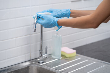 Close up of female hand in protective gloves blue wiping dust using spray and cloth while cleaning her kitchen.Cleaning and housekeeping concept