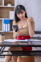 Happy excited business asian woman in office working on laptop computer with mobile phone,Yes great job.