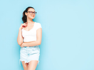 Young beautiful smiling female in trendy summer jeans skirt and top  clothes. carefree woman posing near blue wall in studio. Positive brunette model having fun.Cheerful and happy