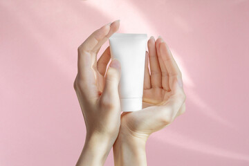 Woman's hands are holding an unmarked plastic container for cosmetics. White bottle for cream,...