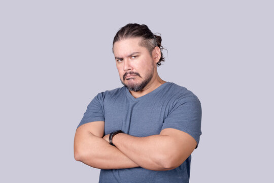 A bitter man in his 30s looks at the camera with a scowling face and arms crossed. Jealousy, displeasure or pettiness.