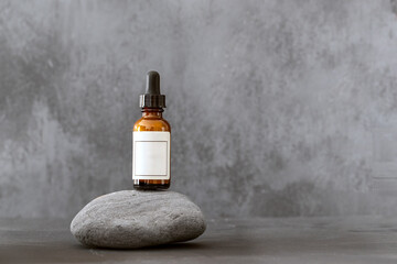 Cosmetic serum bottle with white label on a natural stone on a dark grey background. Mock up packaging