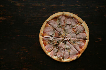 Pizza lies on a dark wooden table. Place for text. View from above. Pizza delivery