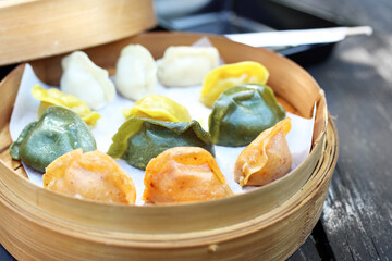Traditional Chinese dumplings in a bamboo steamer basket, close-up. Colorful dim sum cooked on steam.