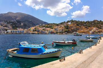 Fototapeta na wymiar Panoramic view of small haven of Symi island. Village with tiny beach, moored boats and colorful houses located on rock. Tops of mountains on Rhodes coast, Greece