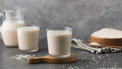 Glasses of vegetable rice milk and a jug on a gray background. Vegetarian food, lactose free milk. 