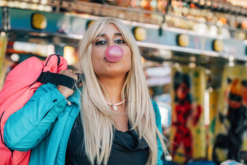 funny girl in amusement park chewing gum and blowing balloons