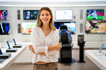 Beautiful young woman choosing which digital device to buy in tech store..