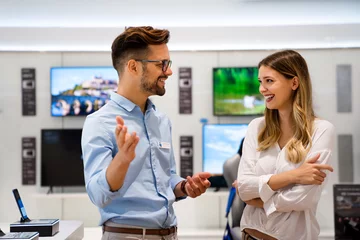 Foto op Canvas Gelukkige verkoper man helpt vrouw om een nieuw digitaal slim apparaat te kopen in de technische winkel. © NDABCREATIVITY