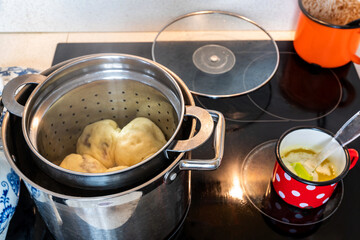 Boiled lum dumplings in open pot on ceramic hob, lid, melted butter in small red dotted pot, closeup.