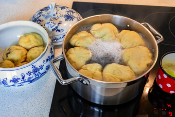Fruit dumpling floating in boiling water on hob, dumpling in bowl, red spotted pot.