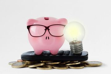 Piggy bank with light bulb on calculator and coins - Concept of electricity and energy saving