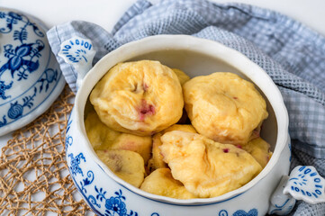 Boiled sweet plum dumpling in bowl, lid, towel, bamboo pad on table.