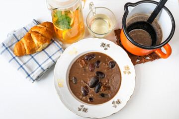 Giant bean soup in plate and in pot, orange drink, bread on towel on white.
