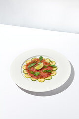 Beef carpaccio with zucchini and cucumber on white table with sunlight shadows. Appetizer of meat - beef carpaccio on summer dining. Sliced raw meat in italian style. Aesthetic menu.