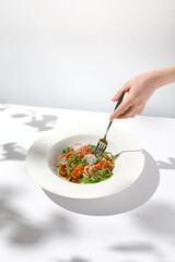 Salmon salad and female hand. Woman eating elegant summer salad. Composition with fish appetizer and fork holding person. Trendy summer food on white background with female hand.