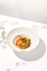 Vegetarian pasta with basil and tomatoes on white plate. Tomato pasta in summer menu with hard shadows Spaghetti with tomatoes on light background. Vegan food - spaghetti marinara