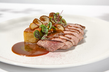 Roasted duck breast with potato gratin and sauce on light background. Fried duck fillet on white plate with hard shadows Elegant summer menu. French cuisine - duck breast with gravy