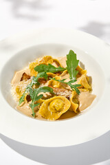 Italian ravioli with meat and mushroom sauce on white plate. Meat tortellini with creamy sauce in summer menu with shadows of tree leaves Ravioli stuffed beef in elegant style
