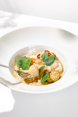 Seafood risotto with scallops and cauliflowers on white plate. Creamy risotto with sea scallops and cauliflowers. Italian risotto with sea scallops on light background with shadows of leaves