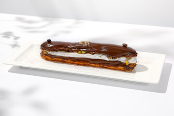 Chocolate eclair on white plate. French dessert stuffed custard cream. Eclair with coffee flavours...